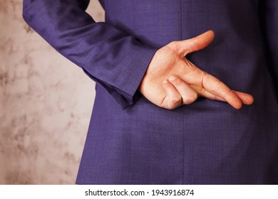 Man In Business Suit Holding Crossed Fingers Behind His Back. Grey Background