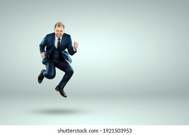 A man in a business suit jumps up cheerfully against a light background. The concept of joy, success, luck, winning