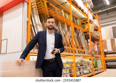 A Man In A Business Suit In A Lumber Store Looks At The Camera With A Smile