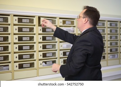 Man In A Business Suit Opens The Mailbox In The Lobby Of Apartment Building 