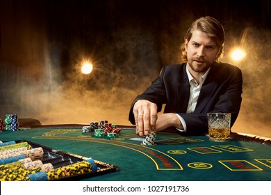 A Man In A Business Suit Sitting At The Game Table. Male Player. Passion, Cards, Chips, Alcohol, Dice, Gambling, Casino - It Is As Male Entertainment.