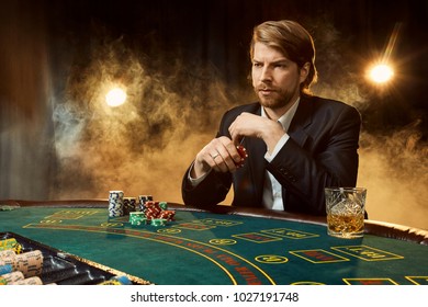 A man in a business suit sitting at the game table. Male player. Passion, cards, chips, alcohol, dice, gambling, casino - it is as male entertainment.