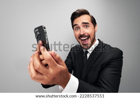 Man businessman holding phone in hand looking into screen video call and selfies and smile with teeth. Close-up wide angle photo gray isolated background