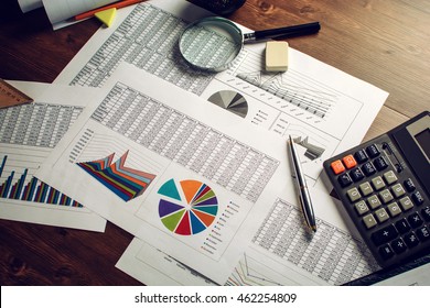 The man (businessman, manager, analyst, student) working with tables, graphs, diagrams, makes calculations at the wooden table in the office in the evening (or at night), after hours