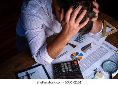 The man (businessman, manager, analyst, student) working with tables, graphs, diagrams, makes calculations at the wooden table in the office in the evening (or at night), after hours - Powered by Shutterstock