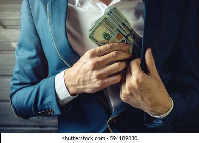 Man businessman, member or officer in a suit puts a bribe in the form of hundred dollar bills in his pocket. the concept of corruption and bribery among high-ranking officials