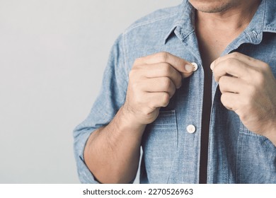 Man buttoning up blue jeans shirt. Studio shot on grey wall background. - Shutterstock ID 2270526963