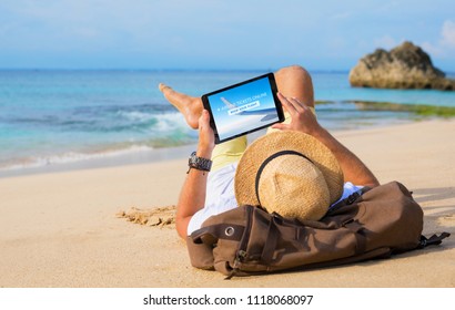 Man buying airline tickets online on tablet while relaxing on beach - Powered by Shutterstock