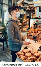 Man Buying Coffee And Cake In The Coffee Shop To Go. Man Standing At Counter Wearing The Face Mask To Avoid Virus Infection And To Prevent The Spread Of Disease In Time Of Coronavirus