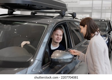 Man Buys A Car At A Car Dealership. A Female Salesperson And Car Rental Helps With The Purchase. Signing A Trade-in Contract And Handing Over Keys, Shaking Hands. A Successful Man Chooses A New Car