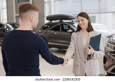 Man Buys A Car At A Car Dealership. A Female Salesperson And Car Rental Helps With The Purchase. Signing A Trade-in Contract And Handing Over Keys, Shaking Hands. A Successful Man Chooses A New Car