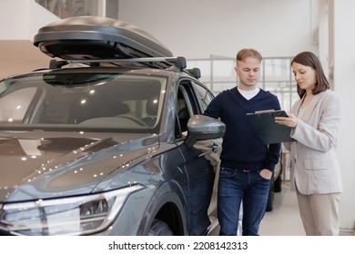 Man Buys A Car At A Car Dealership. A Female Salesperson And Car Rental Helps With The Purchase. Signing A Trade-in Contract And Handing Over Keys, Shaking Hands. A Successful Man Chooses A New Car