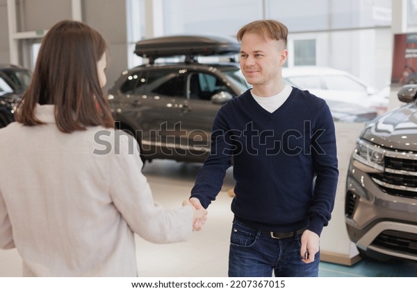 man buys a car at a car dealership. A female
salesperson and car rental helps with the purchase. signing a
trade-in contract and handing over keys, shaking hands. A
successful man chooses a new
car