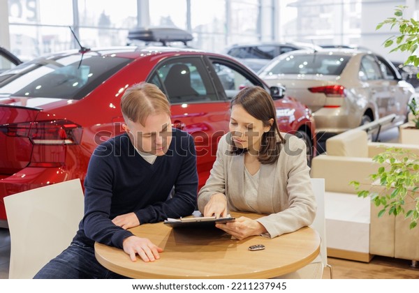 man buys a car at a car dealership. A female
salesperson and car rental helps with the purchase. signing a
trade-in contract and handing over keys, shaking hands. A
successful man chooses a new
car