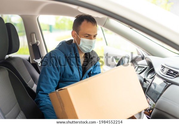Man by the car. Guy in a delivery\
uniform. Man in a medical mask. Coronavirus\
concept.