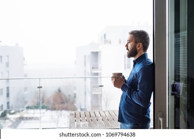 A man by the window holding a cup of coffee at home. - Powered by Shutterstock