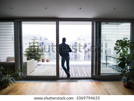 Un hombre cerca de la ventana sosteniendo una taza de café en casa.
