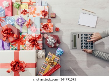 Man Calculating Costs With A Calculator And Lots Of Colorful Gift Boxes, Expensive Christmas Concept