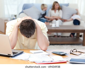 Man Calculating His Bills While His Family Are On The Sofa