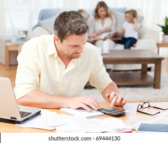 Man Calculating His Bills While His Family Are Sitting On The Sofa