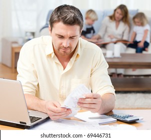 Man Calculating His Bills While His Family Are On The Sofa