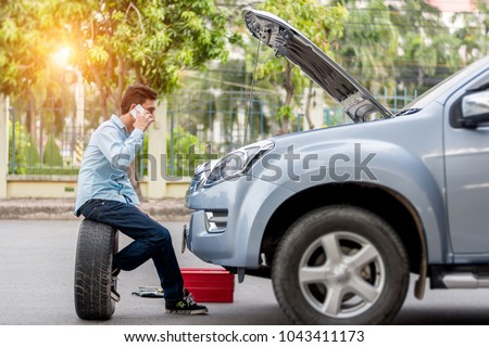 Man call examining a broken car on a sunny day
