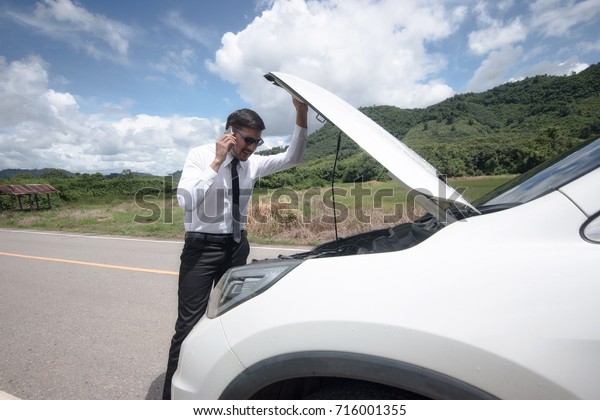 Man call for help on the phone.Are can\
not continue the way because of the broken\
car.