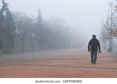 A man with a camera in his hand walking on a foggy red brick sidewalk