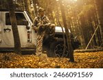 A man in camouflage clothing sitting on his SUV offroad vehicle