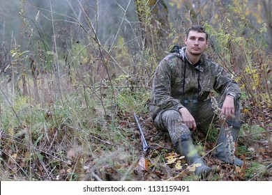 A Man In Camouflage And With Guns In A Forest Belt On A Spring Hunt
