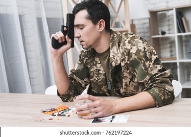 A man in camouflage suffers from depression after returning from the army. He uses alcohol and narcotic tablets. He is tormented by heavy memories. He's holding a gun in his hand.