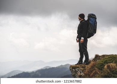 The man with a camping backpack standing on a cliff