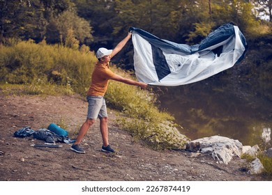 Man camping in nature, setting up the tent for overnight staying near forest river. - Powered by Shutterstock