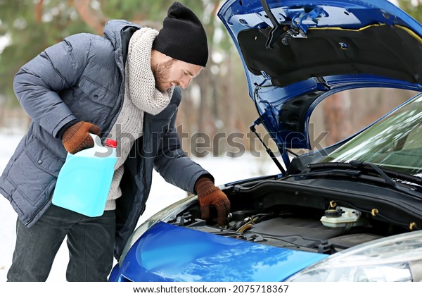 Man\
with canister of petroleum near car on winter\
day