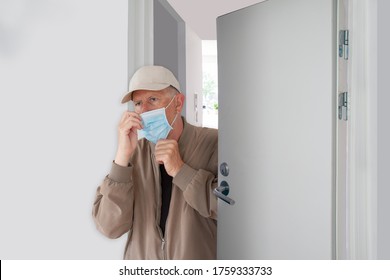 Man with cap adjusting his protective medical mask as he leaves home. He walks out a half opened door in a building. Coronavirus Covid-19 pandemic make it important to wear a mask when you go out.  - Powered by Shutterstock