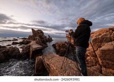 A man capturing photos of the Mediterranean Sea with his camera and tripod at sunrise. Costa Brava, Cala Rosamar - Powered by Shutterstock