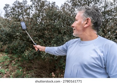 Man capturing selfie using stick and smartphone outdoors