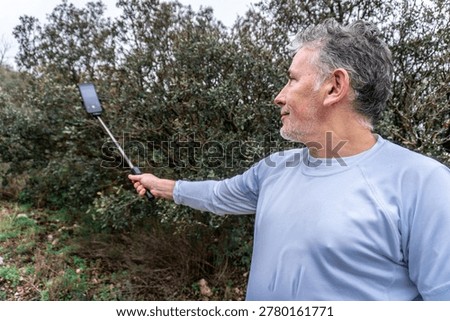 Man capturing selfie using stick and smartphone outdoors