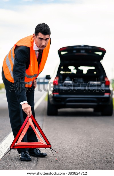 Man\
with car breakdown erecting warning triangle on\
road