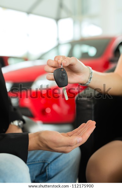 Man at a
car dealership buying an auto, the female sales rep giving him the
key, macro shot with focus on hands and
key
