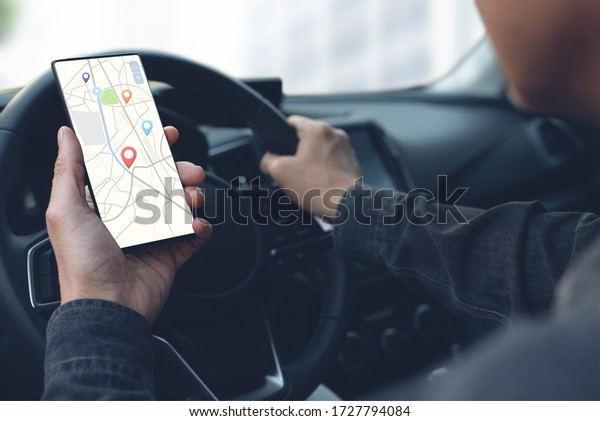 Man in car, driver\
using black mobile smart phone searching location with pin on map\
gps navigation, locator application display, transportation\
technology concept