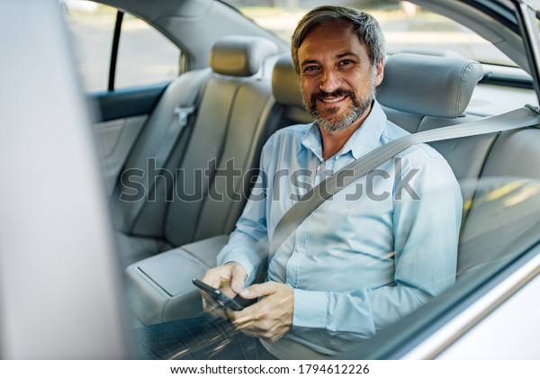 Man in a car, grey background, driving by\
personal driver.