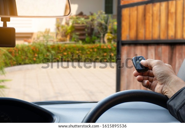 Man in car, hand using remote
control to open the automatic gate when arrived home. The auto
electric door, home remote control and security system  concept.
