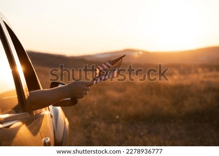 Man in the car holding american USA flag in the sunset. Independence Day or traveling in America concept.