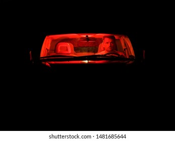 A Man In A Car With A Red Light Inside On A Dark Night. Front View.