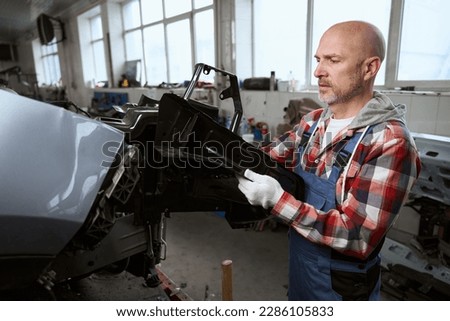 Man in car repair shop disassembles broken car for parts