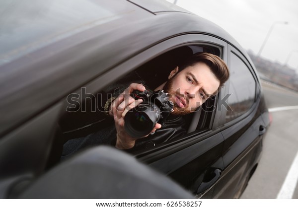 The man in the car reviews the\
photos on the camera. Spy, paparazzi, journalist,\
photographer.