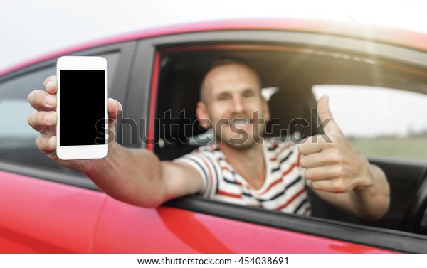 Man in car showing smart phone display and\
showing thumb up. Focus on mobile\
phone.
