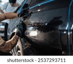 Man car washer washes car and wipes black car with rag in detailing studio