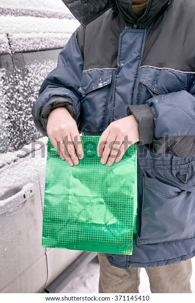 Man carefully holding a green bag near the car,\
vertical cropped shot